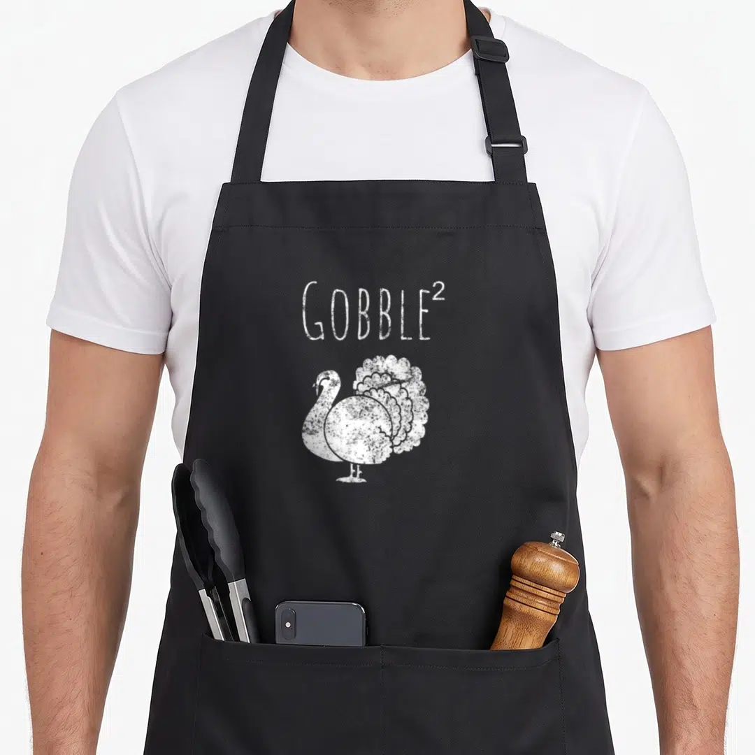 Squared thanksgiving day aprons - Distressed white GOBBLE² text above a line art turkey — shown on a black cotton canvas apron against a white background
