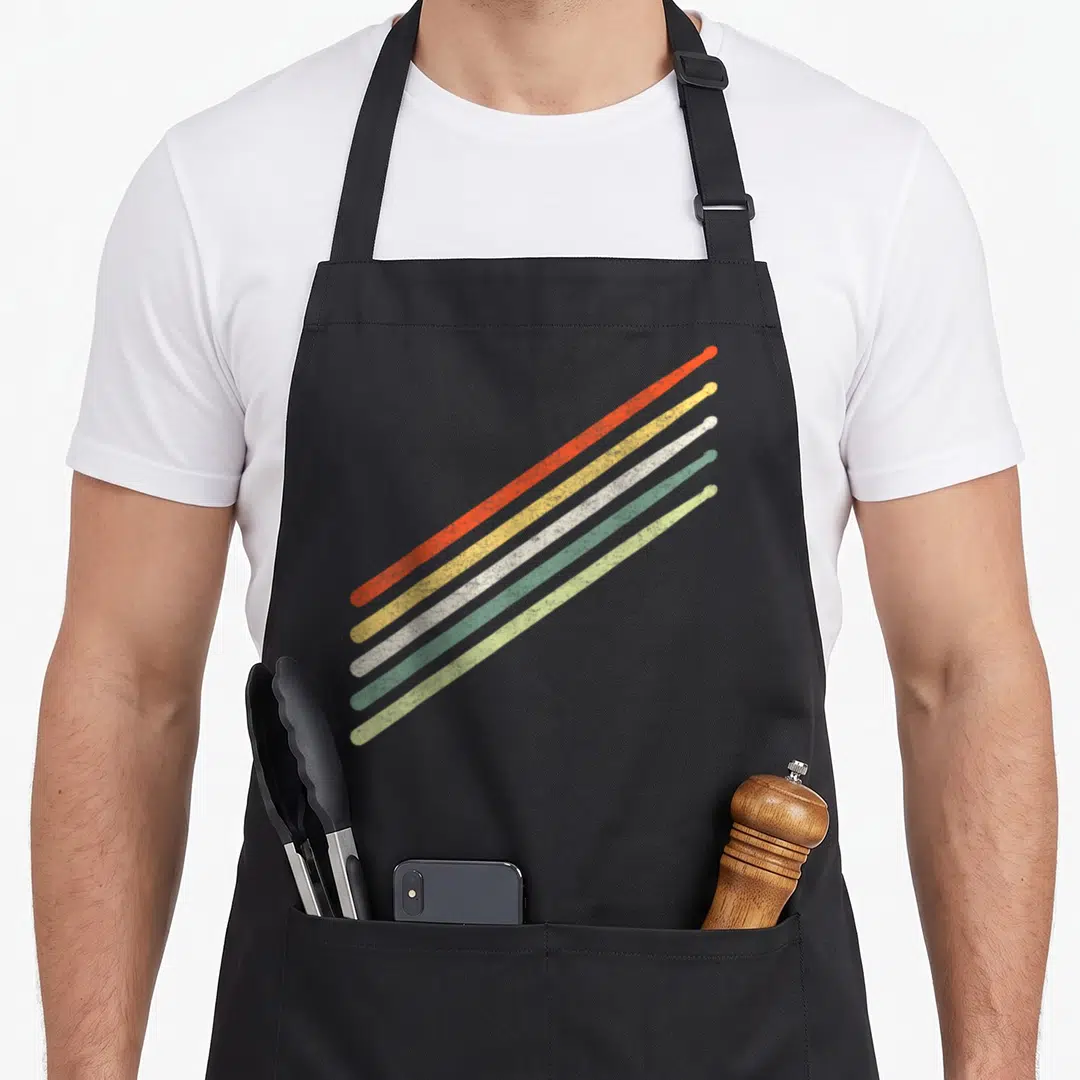 Drummer pigeon vintage apron - Five diagonal drumsticks in red yellow white green and light green with distressed — shown on a black cotton canvas apron against a white background