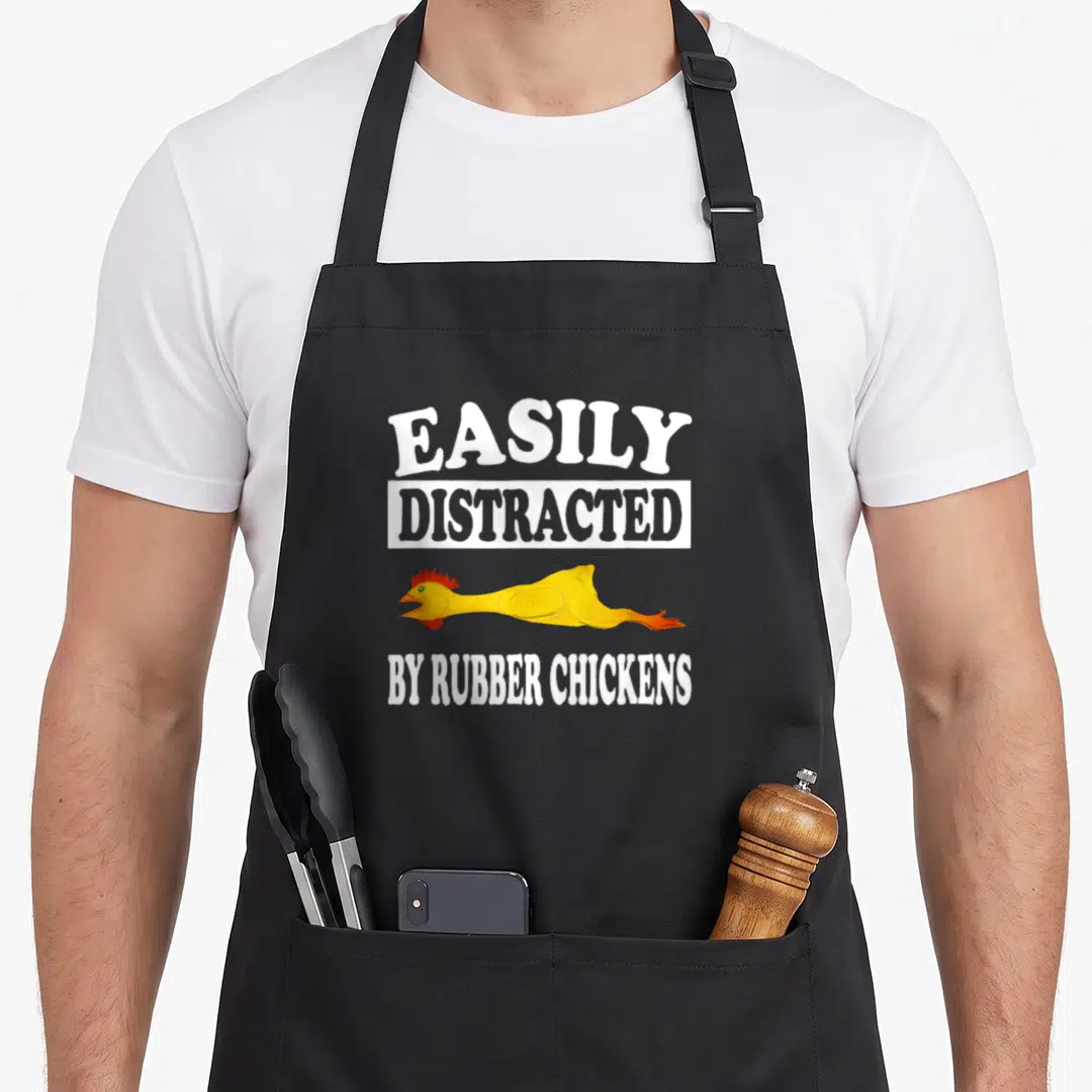 Easily chicken apron - Yellow rubber chicken between white text EASILY DISTRACTED BY RUBBER CHICKENS — shown on a black cotton canvas apron against a white background