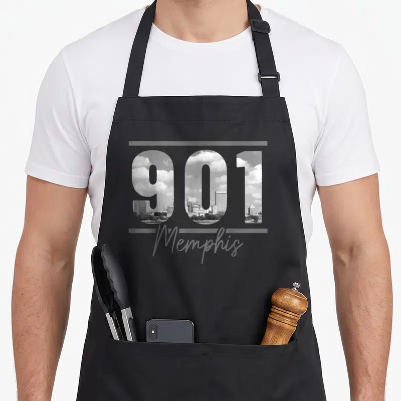 Area memphis apron - 901 numbers filled with grayscale skyline photo above Memphis script between grey bars — shown on a black cotton canvas apron against a white background