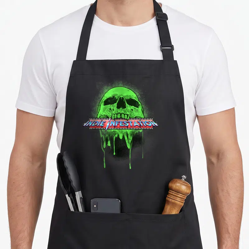 Infestation indie apron - Green skull with slime and film strip reading INDIE INFESTATION in blue and red — shown on a black cotton canvas apron against a white background