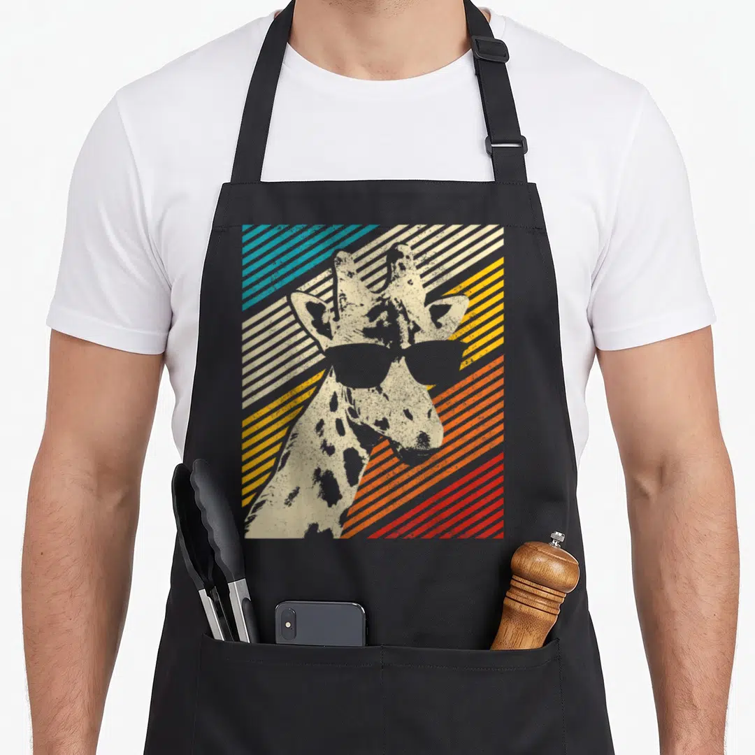 Funny sunglass giraffe apron - Beige giraffe wearing sunglasses against blue yellow orange and red diagonal stripes — shown on a black cotton canvas apron against a white background