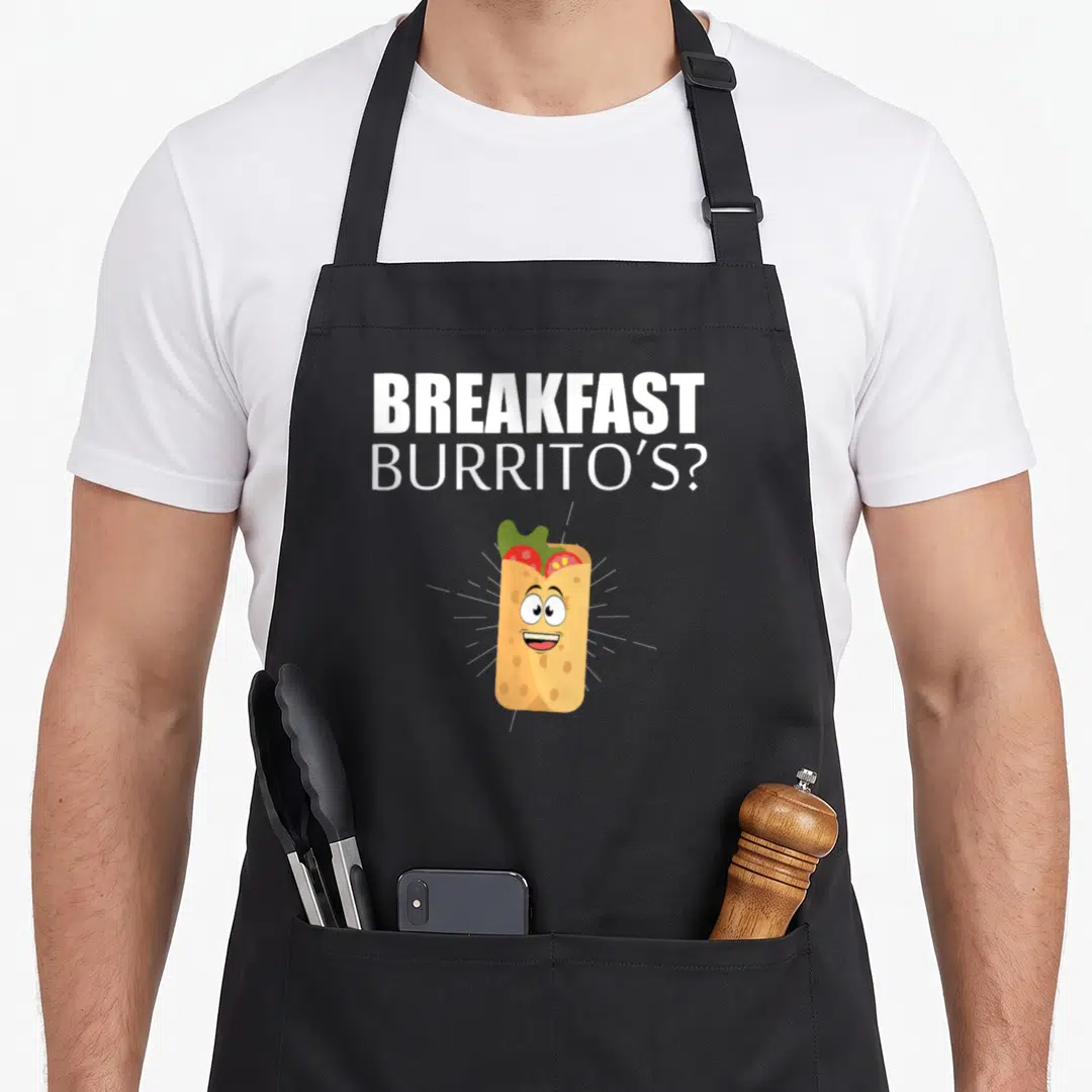 Breakfast mexican apron - Cartoon burrito with face and white text BREAKFAST BURRITO'S? in tan green and red — shown on a black cotton canvas apron against a white background