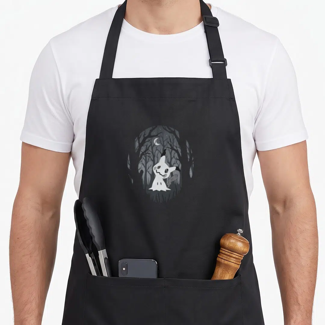 Fairy spooky apron - Cartoon ghost creature in grey and white circular vignette with dark forest and crescent moon — shown on a black cotton canvas apron against a white background