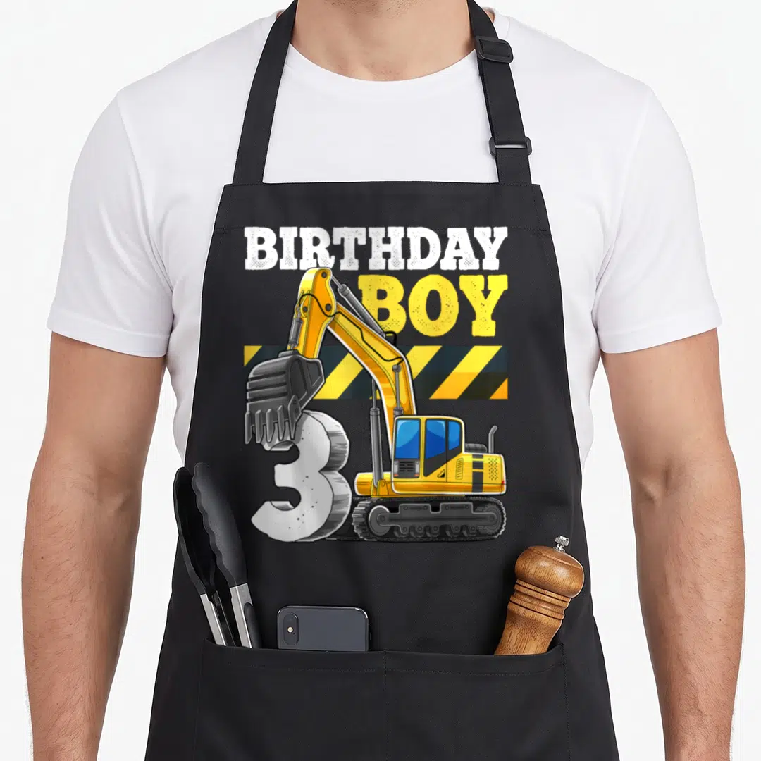 Birthday vehicle apron - Cartoon excavator bucket on number 3 with BIRTHDAY BOY text and yellow black stripes — shown on a black cotton canvas apron against a white background
