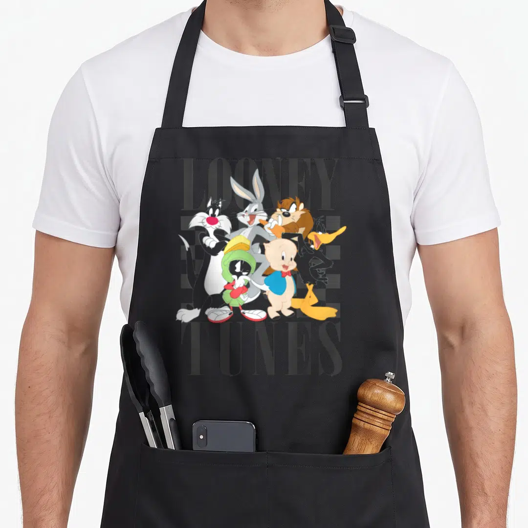 Shot 90s apron - Clustered Looney Tunes characters over grey background with LOONEY TUNES text in black — shown on a black cotton canvas apron against a white background