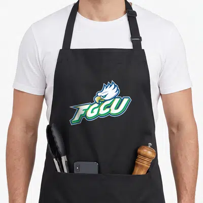 Florida eagles apron - Cartoon eagle head behind slanted FGCU text in white blue green and yellow — shown on a black cotton canvas apron against a white background
