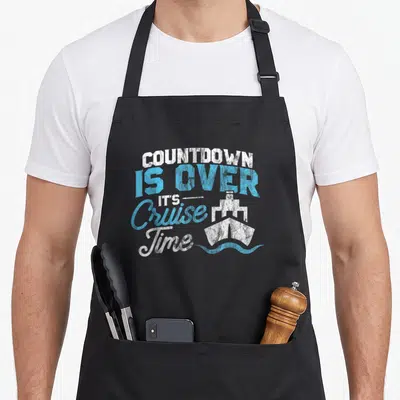 Vintage cruise countdown apron - Distressed text COUNTDOWN IS OVER IT'S Cruise Time next to white ship on blue waves — shown on a black cotton canvas apron against a white background