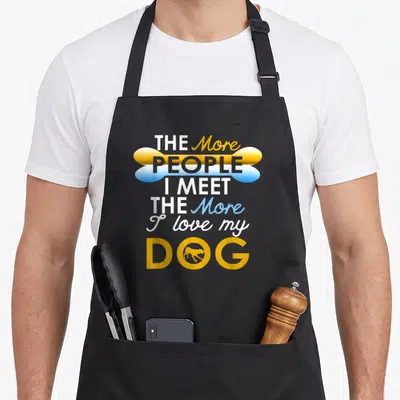 Vintage meet dog apron - Stacked text reading THE More PEOPLE I MEET THE More I love my DOG with a bone graphic and dog — shown on a black cotton canvas apron against a white background