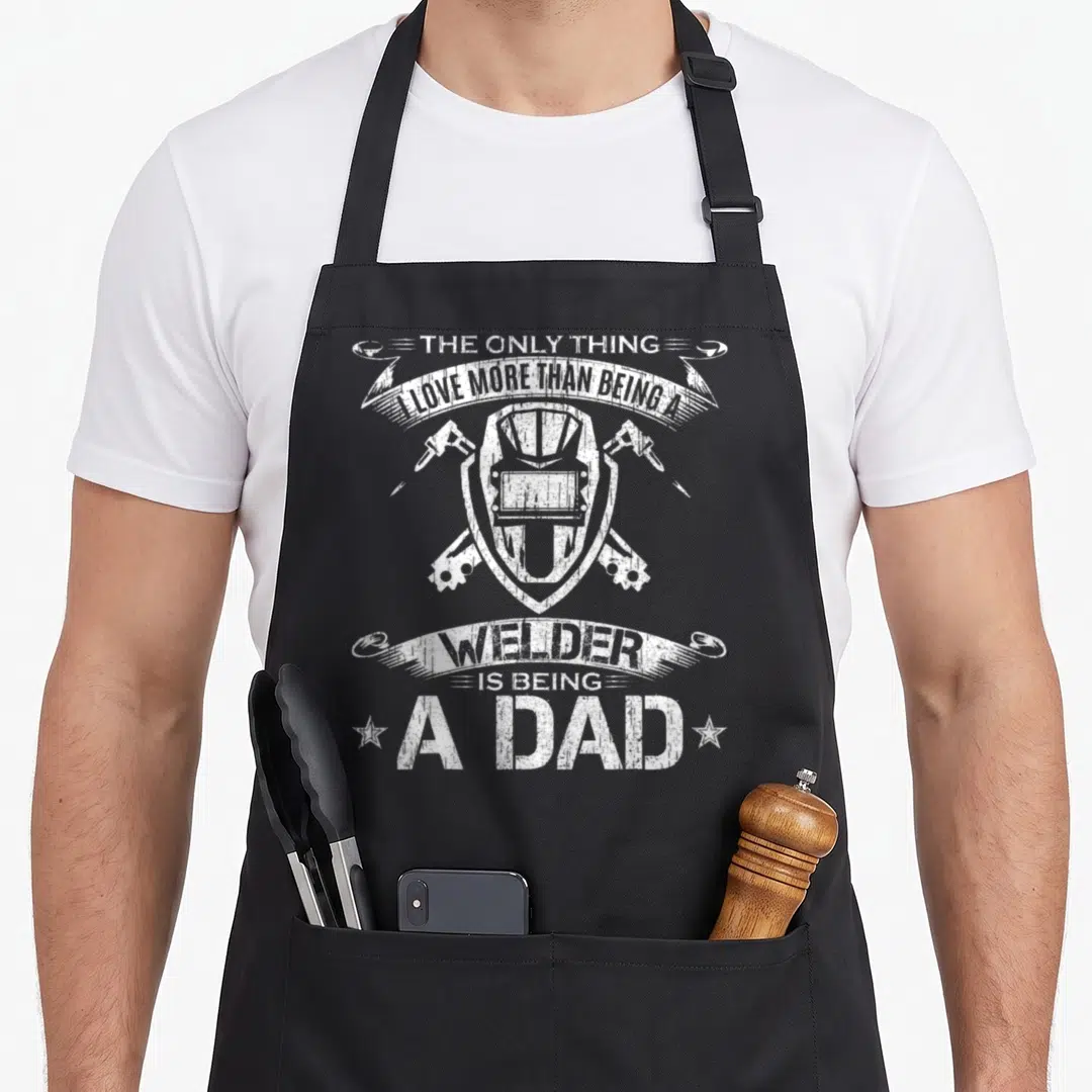 Funny welding welder dad apron - White distressed welding helmet and crossed torches with arched banner text — shown on a black cotton canvas apron against a white background