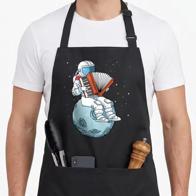 Music accordion player apron - Cartoon astronaut in white suit plays red accordion sitting on light blue moon — shown on a black cotton canvas apron against a white background
