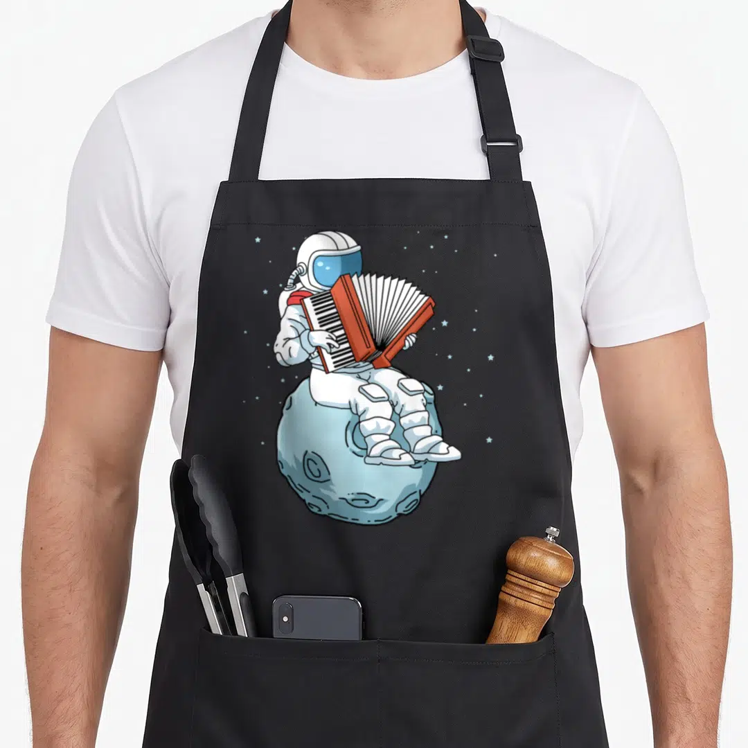 Music accordion player apron - Cartoon astronaut in white suit plays red accordion sitting on light blue moon — shown on a black cotton canvas apron against a white background