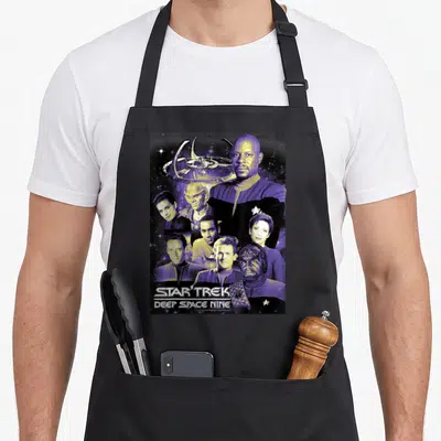 Ds9 crew apron - Photo collage of Deep Space Nine cast members with space station and stacked title text — shown on a black cotton canvas apron against a white background