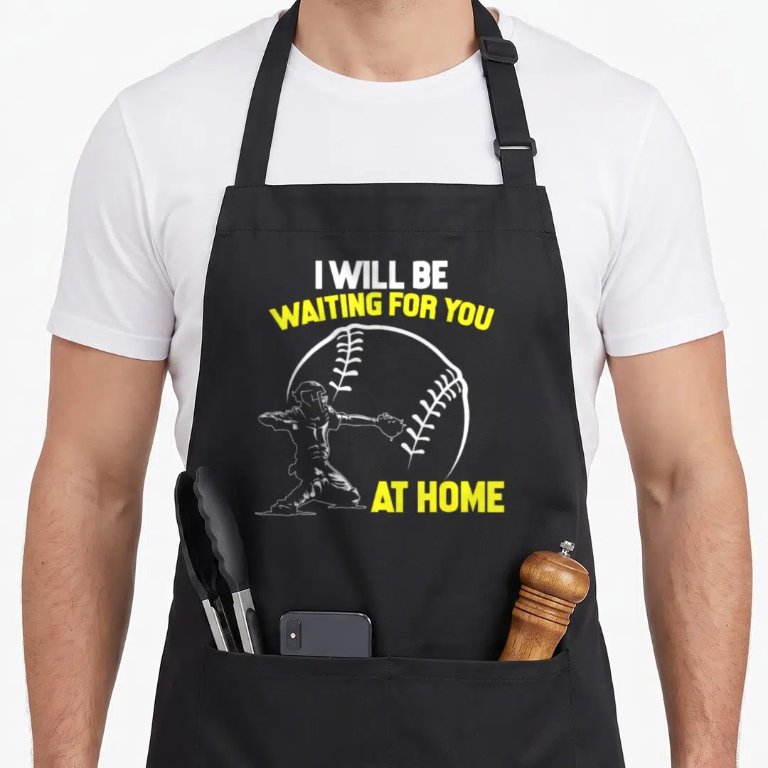 Softball at home aprons - I WILL BE WAITING FOR YOU AT HOME text with baseball outline and catcher silhouette — shown on a black cotton canvas apron against a white background