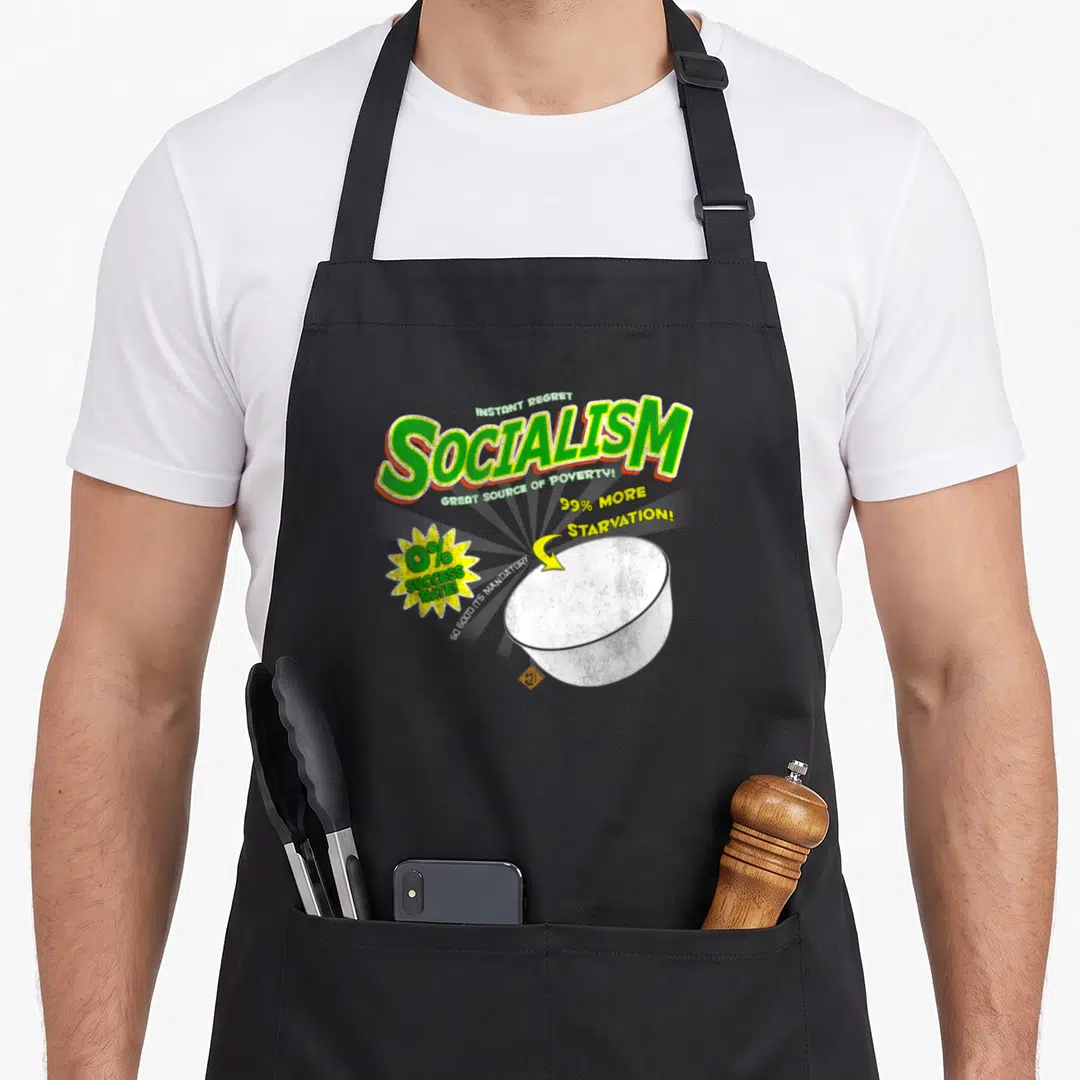 Socialism box apron - Green SOCIALISM text, empty white bowl, yellow starburst, and sarcastic slogans on a cartoon — shown on a black cotton canvas apron against a white background