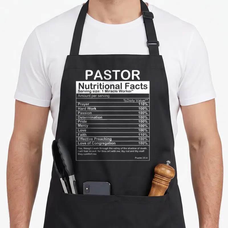 Appreciation pastor apron - White nutrition facts label design listing pastor virtues like prayer, faith, and love — shown on a black cotton canvas apron against a white background
