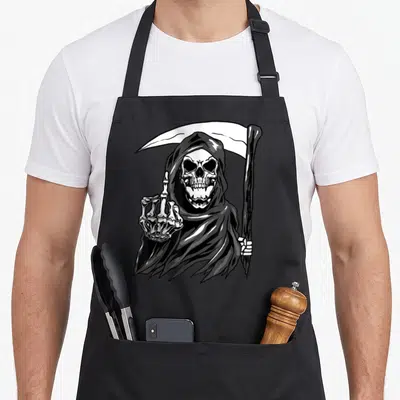 Grim angels and aprons - Realistic Grim Reaper in black and white holding a scythe and raising a middle finger — shown on a black cotton canvas apron against a white background
