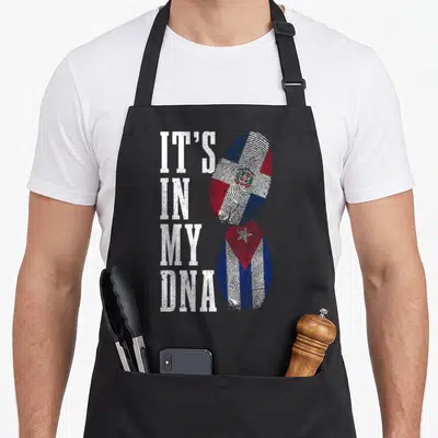 Cuba dominican pride apron - IT'S IN MY DNA text next to Dominican and Cuban flag fingerprints — shown on a black cotton canvas apron against a white background