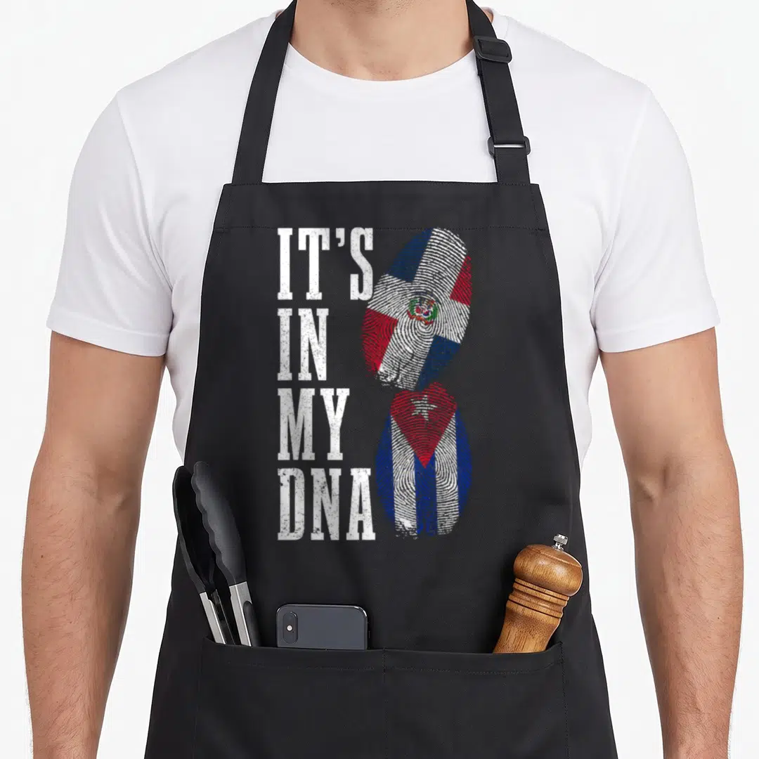 Cuba dominican pride apron - IT'S IN MY DNA text next to Dominican and Cuban flag fingerprints — shown on a black cotton canvas apron against a white background