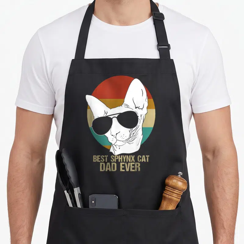 Father cat apron - White sphynx cat with sunglasses over red orange and teal stripes with best sphynx cat dad ever text — shown on a black cotton canvas apron against a white background
