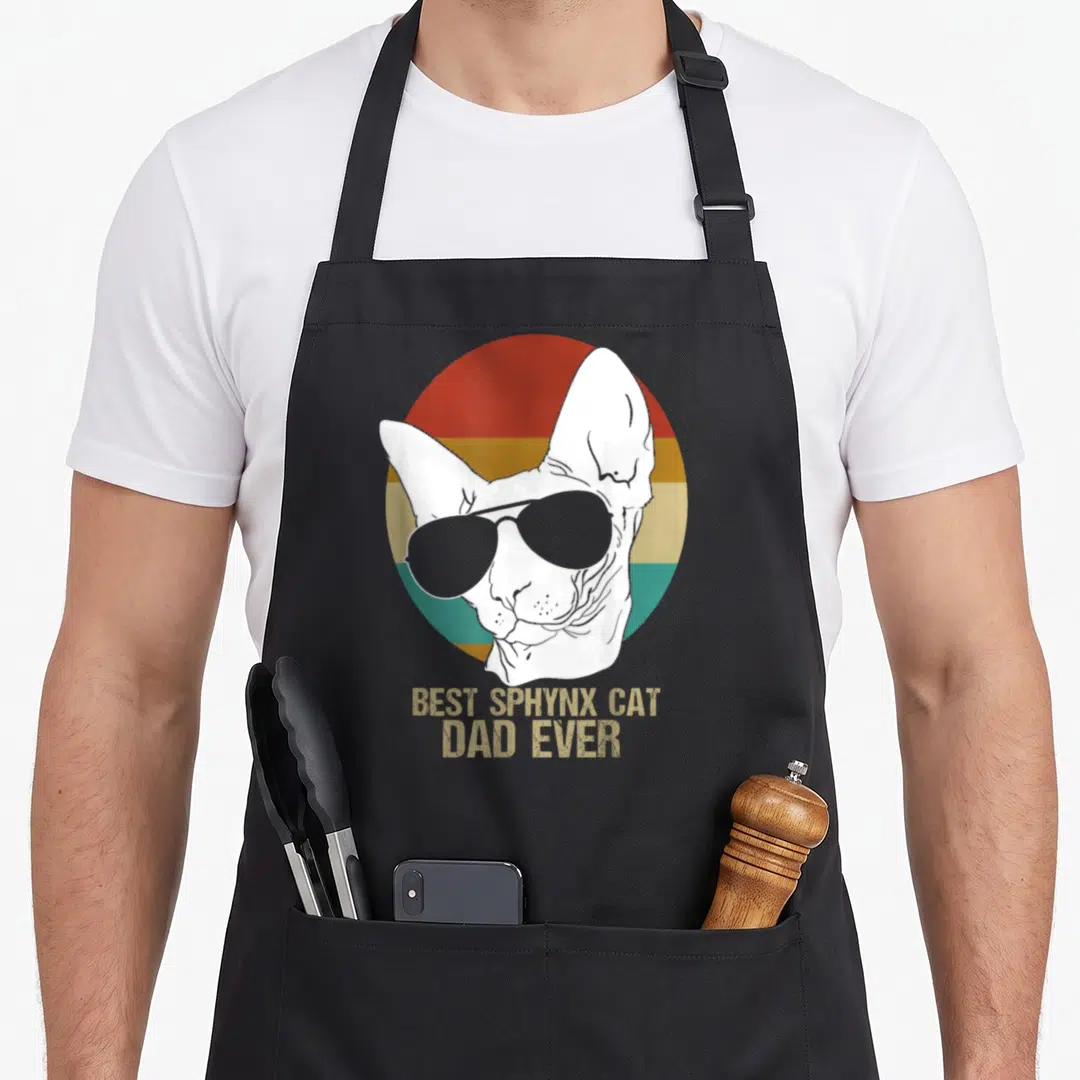 Father cat apron - White sphynx cat with sunglasses over red orange and teal stripes with best sphynx cat dad ever text — shown on a black cotton canvas apron against a white background