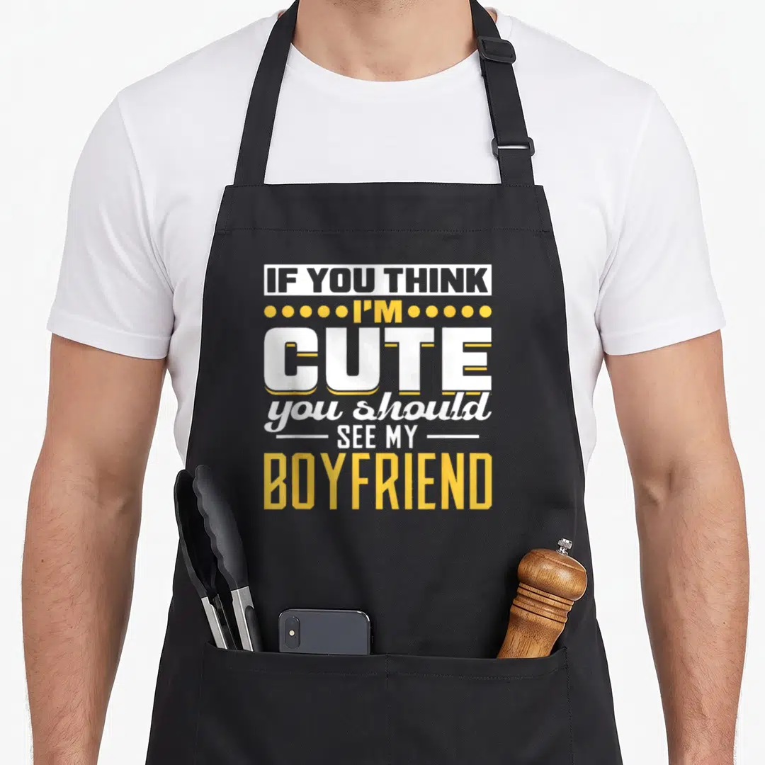 Should find aprons - Stacked white and yellow text reading If You Think I'm Cute You Should See My Boyfriend with dot — shown on a black cotton canvas apron against a white background