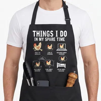 Spare chicken apron - Six cartoon chicken vignettes with text Feed Look Research Talk Think Dream — shown on a black cotton canvas apron against a white background
