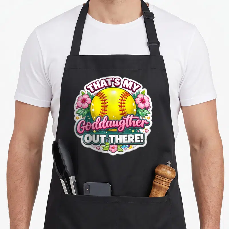 Proud goddaughter apron - Yellow softball with pink flowers and green leaves surrounding arched text — shown on a black cotton canvas apron against a white background