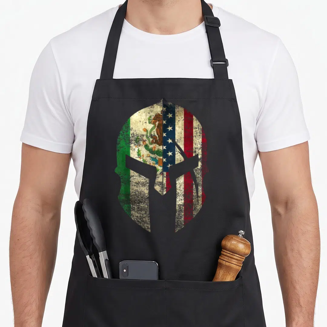 Spartan mexican apron - Distressed spartan helmet filled with split Mexican and American flags in green white red blue — shown on a black cotton canvas apron against a white background