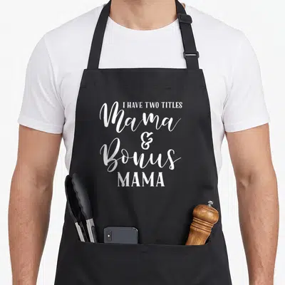 Step mother's day aprons - White text reading I Have Two Titles Mama Bonus MAMA stacked centrally — shown on a black cotton canvas apron against a white background