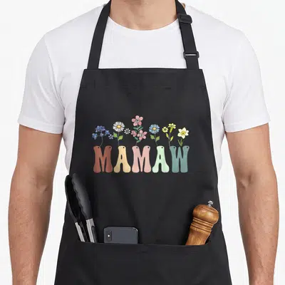 Mamaw floral apron - Colorful wildflowers growing out of the word MAMAW in cartoon style — shown on a black cotton canvas apron against a white background