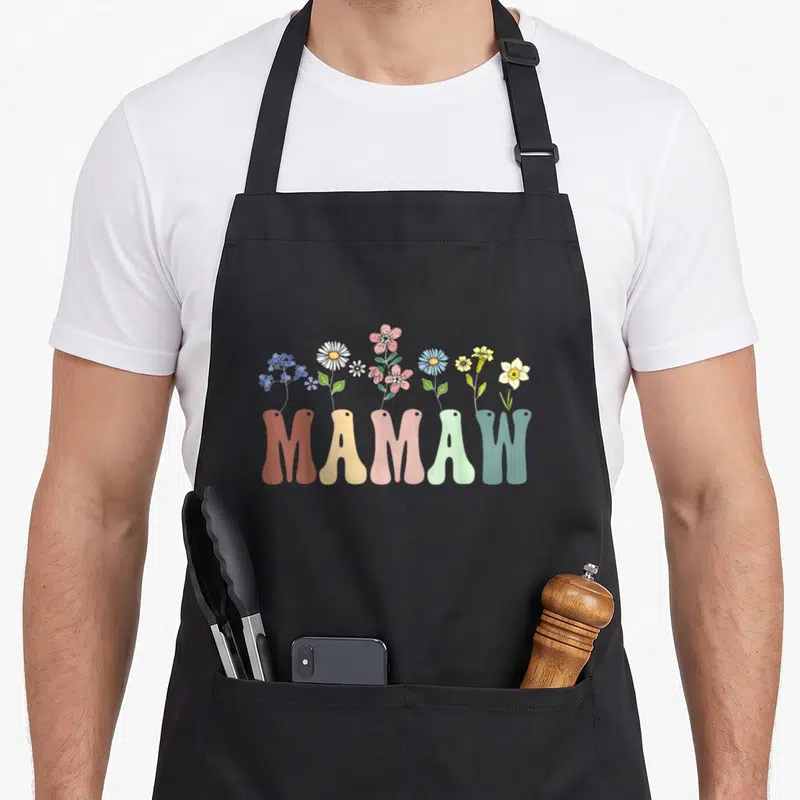 Mamaw floral apron - Colorful wildflowers growing out of the word MAMAW in cartoon style — shown on a black cotton canvas apron against a white background