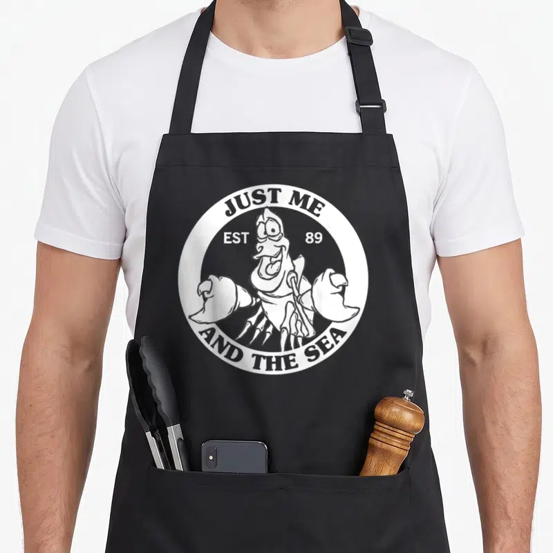 Sebastian flounder apron - White circular logo with grey lobster and text Just Me Est 89 And The Sea — shown on a black cotton canvas apron against a white background