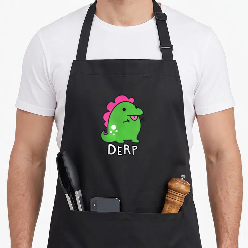 Derpy dinosaur apron - Green cartoon dinosaur with pink crest and white DERP text below — shown on a black cotton canvas apron against a white background