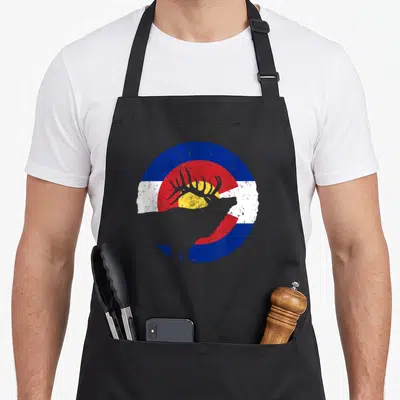 Colorado hunter apron - Grey elk silhouette over distressed circular blue red white and yellow flag design — shown on a black cotton canvas apron against a white background