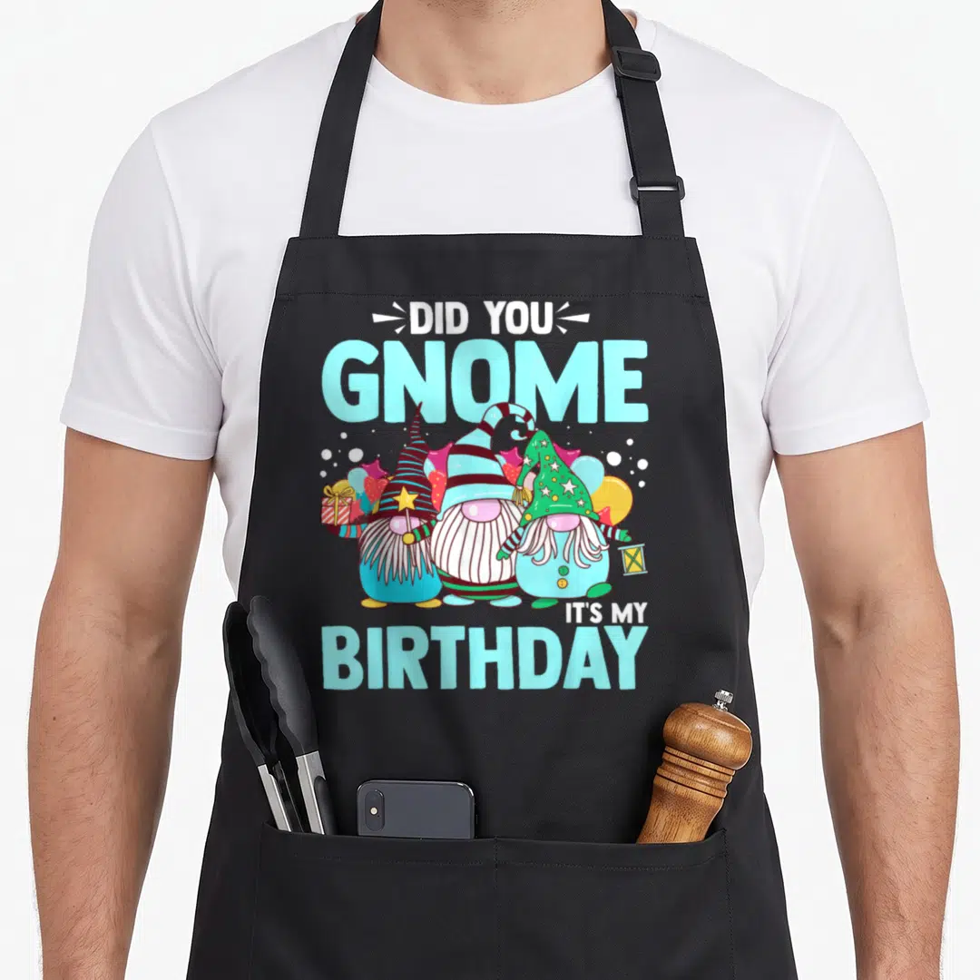 Gnome birthday apron - Three cartoon gnomes with balloons and gift under Did You Gnome It's My Birthday text — shown on a black cotton canvas apron against a white background