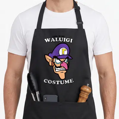 Waluigi halloween white apron - Cartoon Waluigi head with purple hat and text THIS IS MY WALUIGI COSTUME — shown on a black cotton canvas apron against a white background