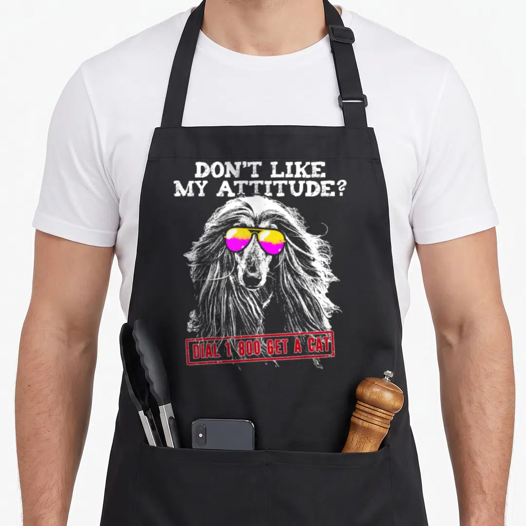 Afghan attitude aprons - Long-haired dog with yellow and pink sunglasses and sarcastic text about dogs versus cats — shown on a black cotton canvas apron against a white background