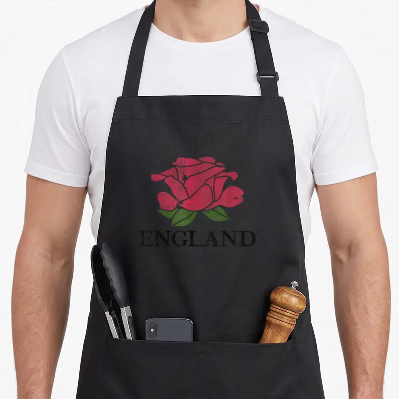 Distressed england rugby apron - Red rose with two green leaves above black ENGLAND text in distressed style — shown on a black cotton canvas apron against a white background