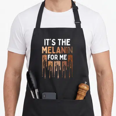 Melanated kwanzaa apron - IT'S THE MELANIN FOR ME text with brown gradient and paint drips — shown on a black cotton canvas apron against a white background