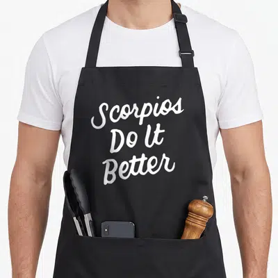 Better zodiac aprons - White stacked script text reading Scorpios Do It Better on black fabric — shown on a black cotton canvas apron against a white background