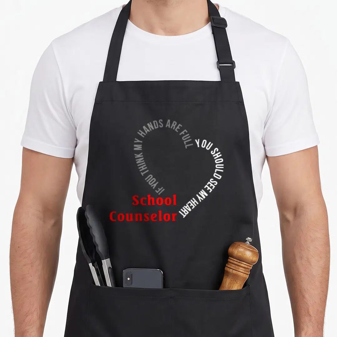 Should counselor apron - White text in a heart shape with red School Counselor label at bottom left — shown on a black cotton canvas apron against a white background