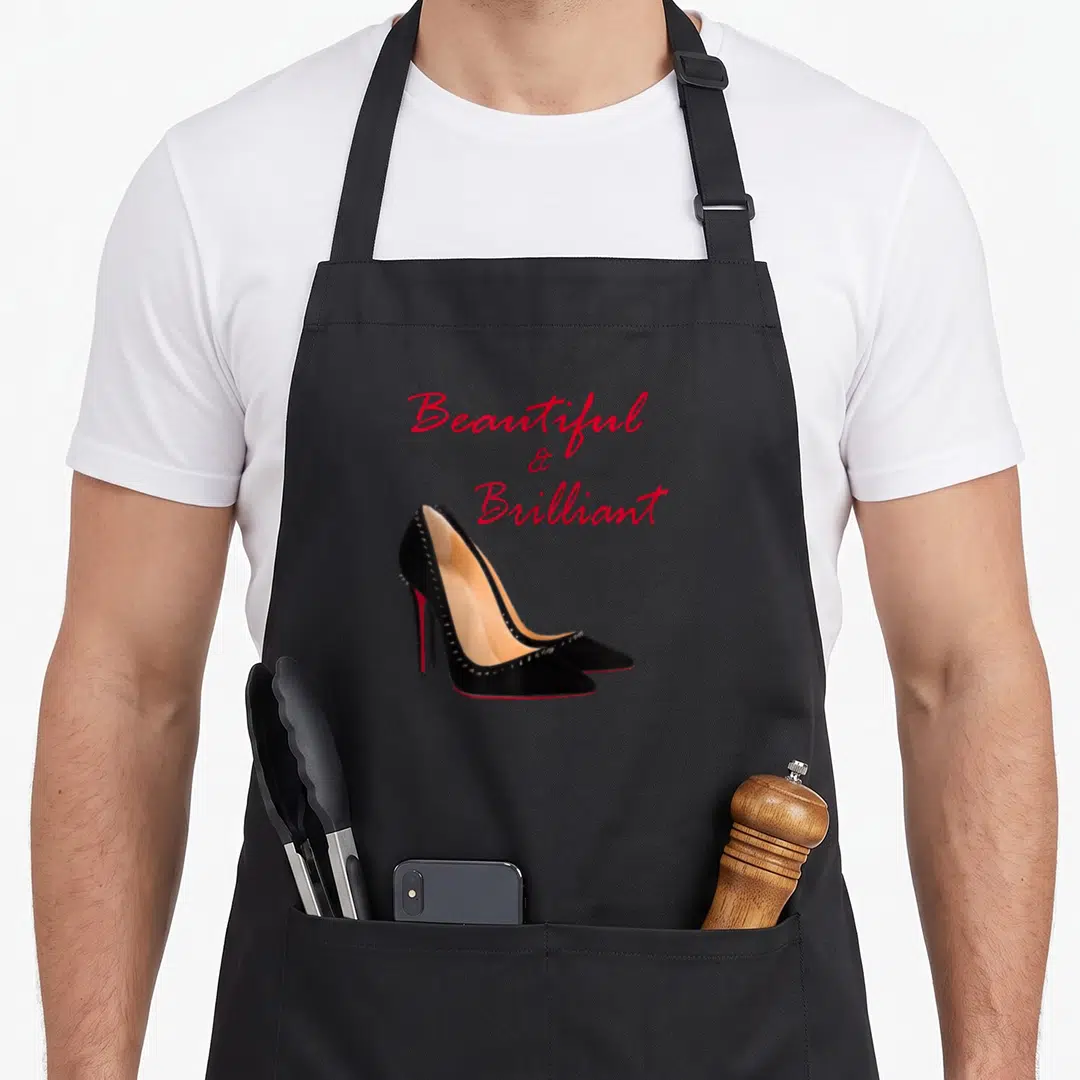 Brilliant beautiful apron - Red script Beautiful & Brilliant above black studded high heels — shown on a black cotton canvas apron against a white background