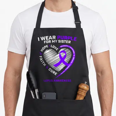 Sister lupus awareness apron - Purple ribbon in white hatched heart with I wear purple for my sister text — shown on a black cotton canvas apron against a white background