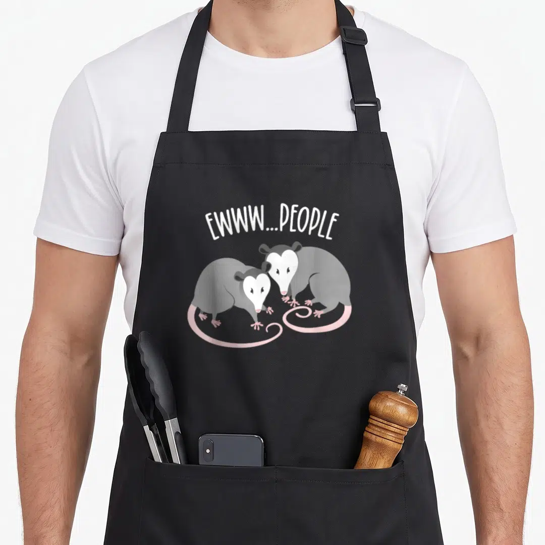Drama opossum apron - Two grey cartoon opossums facing forward under arched white text EWWW...PEOPLE with pink tails — shown on a black cotton canvas apron against a white background
