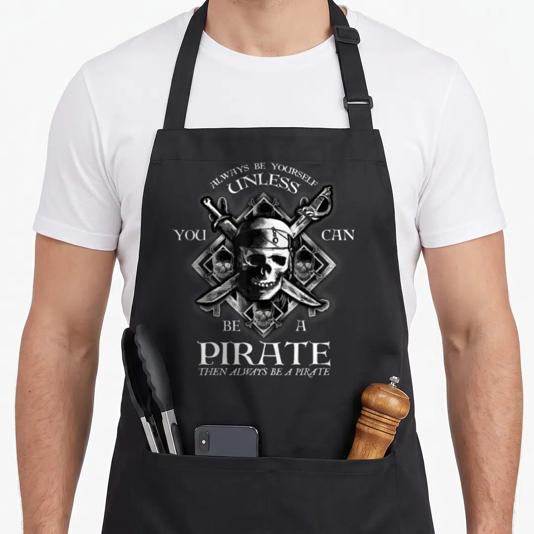 Pirate always yourself apron - Skull with crossed swords inside diamond frame and arched text in white, black, and grey — shown on a black cotton canvas apron against a white background