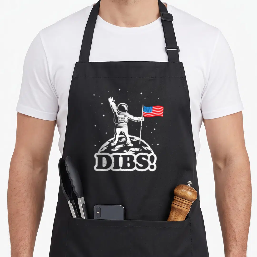 Moon space astronaut lover co apron - Distressed astronaut on moon holding USA flag with DIBS text banner — shown on a black cotton canvas apron against a white background