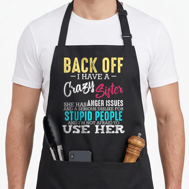 Sibling family aprons - Back Off I Have a Crazy Sister typography in yellow, white, pink, and cyan — shown on a black cotton canvas apron against a white background