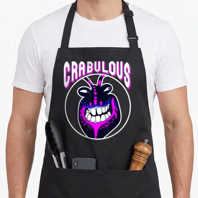 Tamatoa face apron - CRABULOUS text arching over pink and black cartoon crab head in white circle — shown on a black cotton canvas apron against a white background