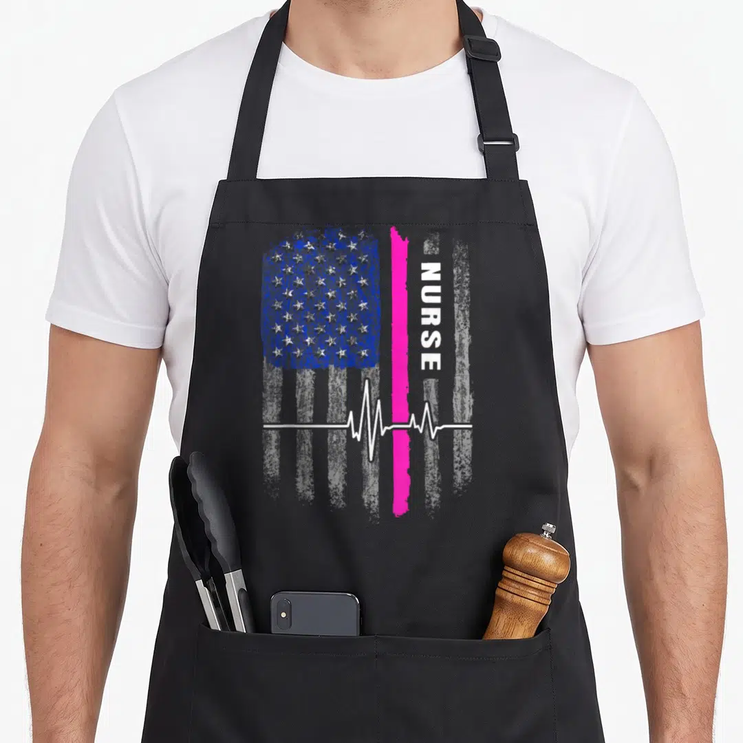Flag nursing apron - Distressed flag with pink stripe, vertical NURSE text, white heartbeat line on black bib — shown on a black cotton canvas apron against a white background
